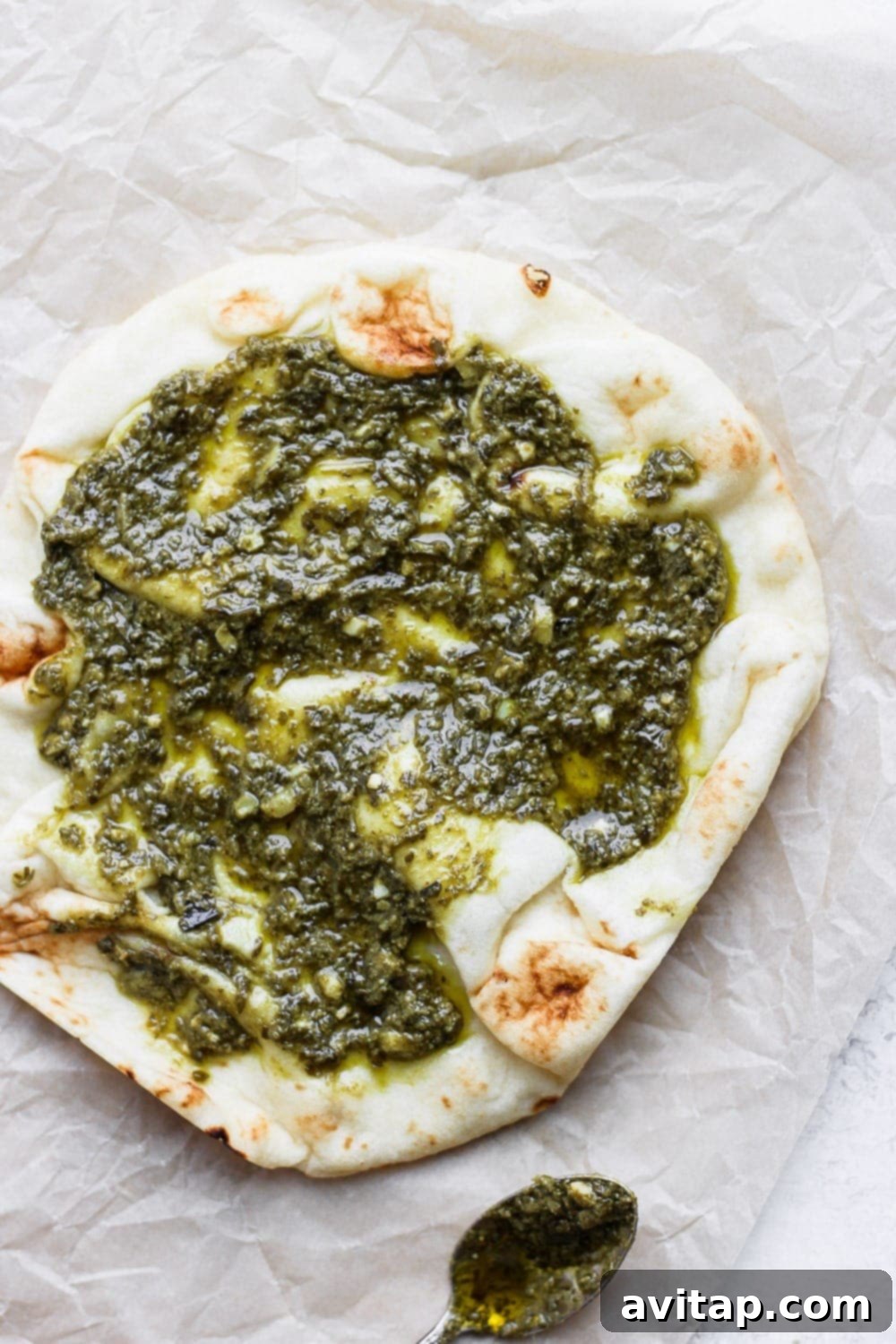 Morning Naan Pizza 4 A delicious Naan pizza generously topped with vibrant green pesto, ready for the oven or additional toppings.