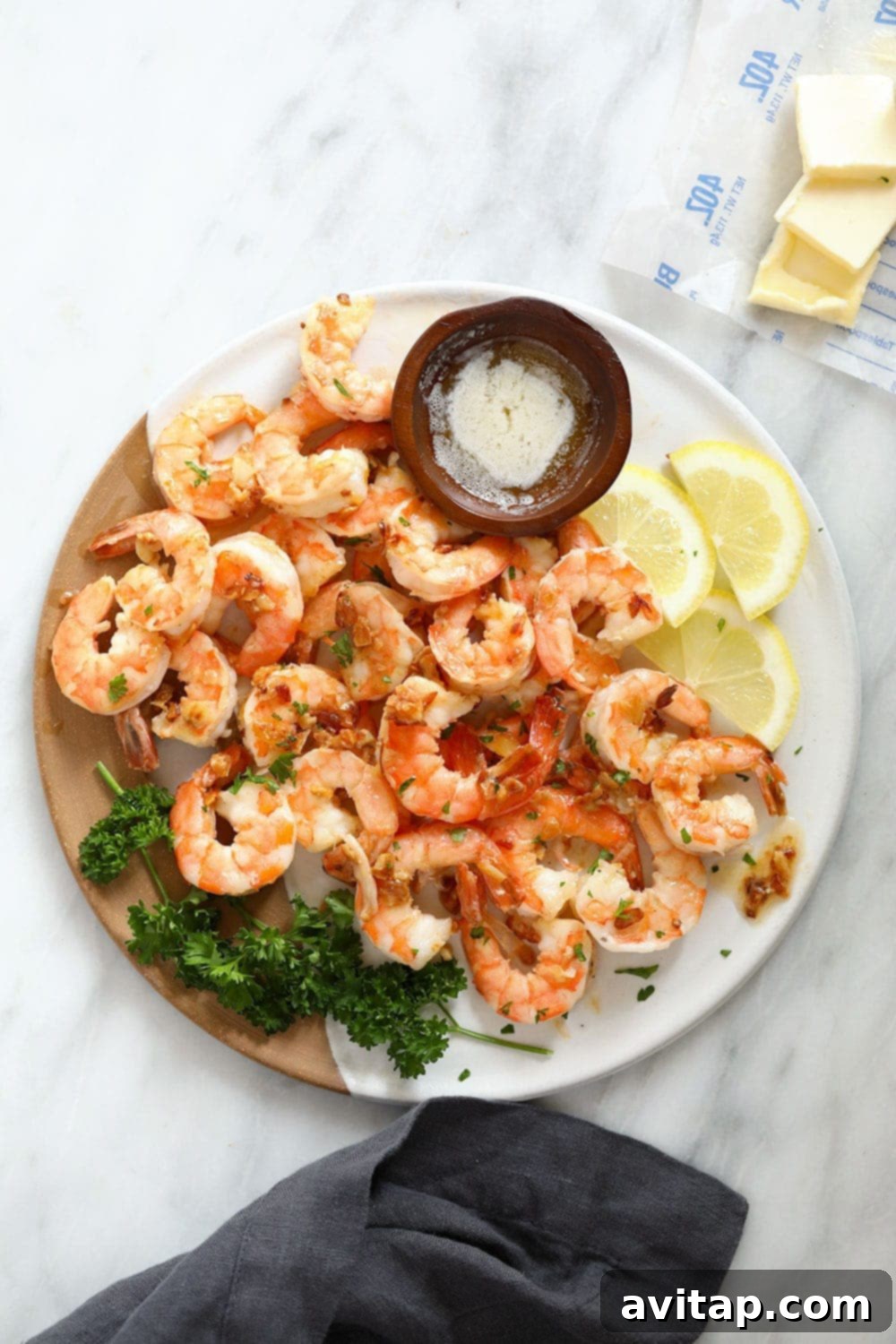 Close-up of freshly cooked garlic butter shrimp on a white plate, garnished with vibrant green parsley and bright lemon slices.