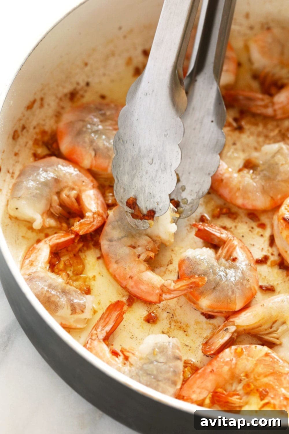 Garlic butter shrimp sizzling in a hot skillet, being skillfully flipped with tongs, showcasing their vibrant pink color.