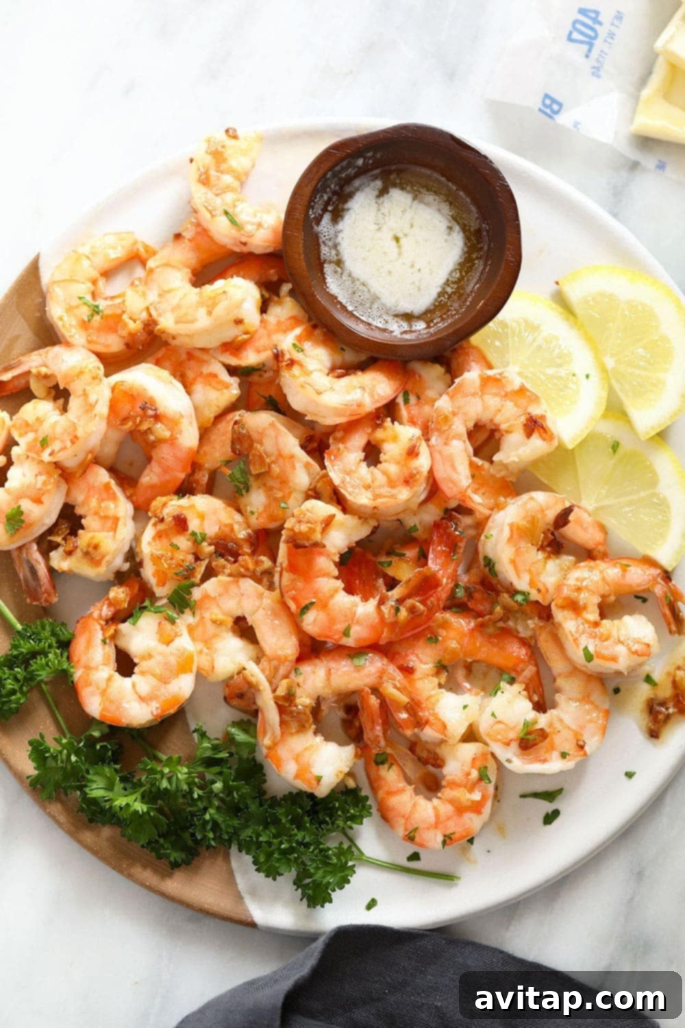 A plate of golden-brown garlic butter shrimp with a small bowl of melted butter for dipping and fresh lemon wedges.