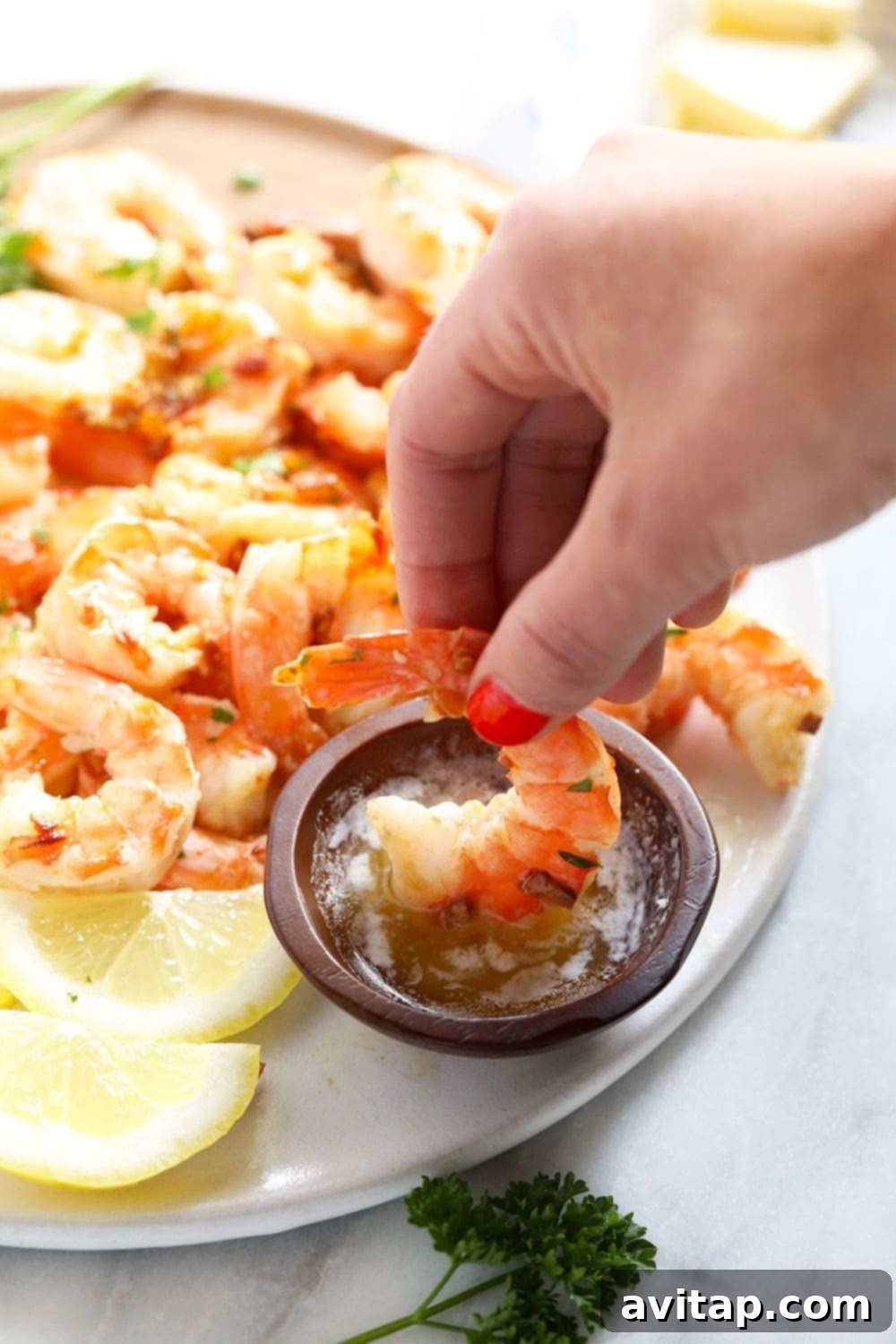 Close-up of a single garlic butter shrimp being dipped into a small white bowl of melted butter, highlighting its juicy texture.