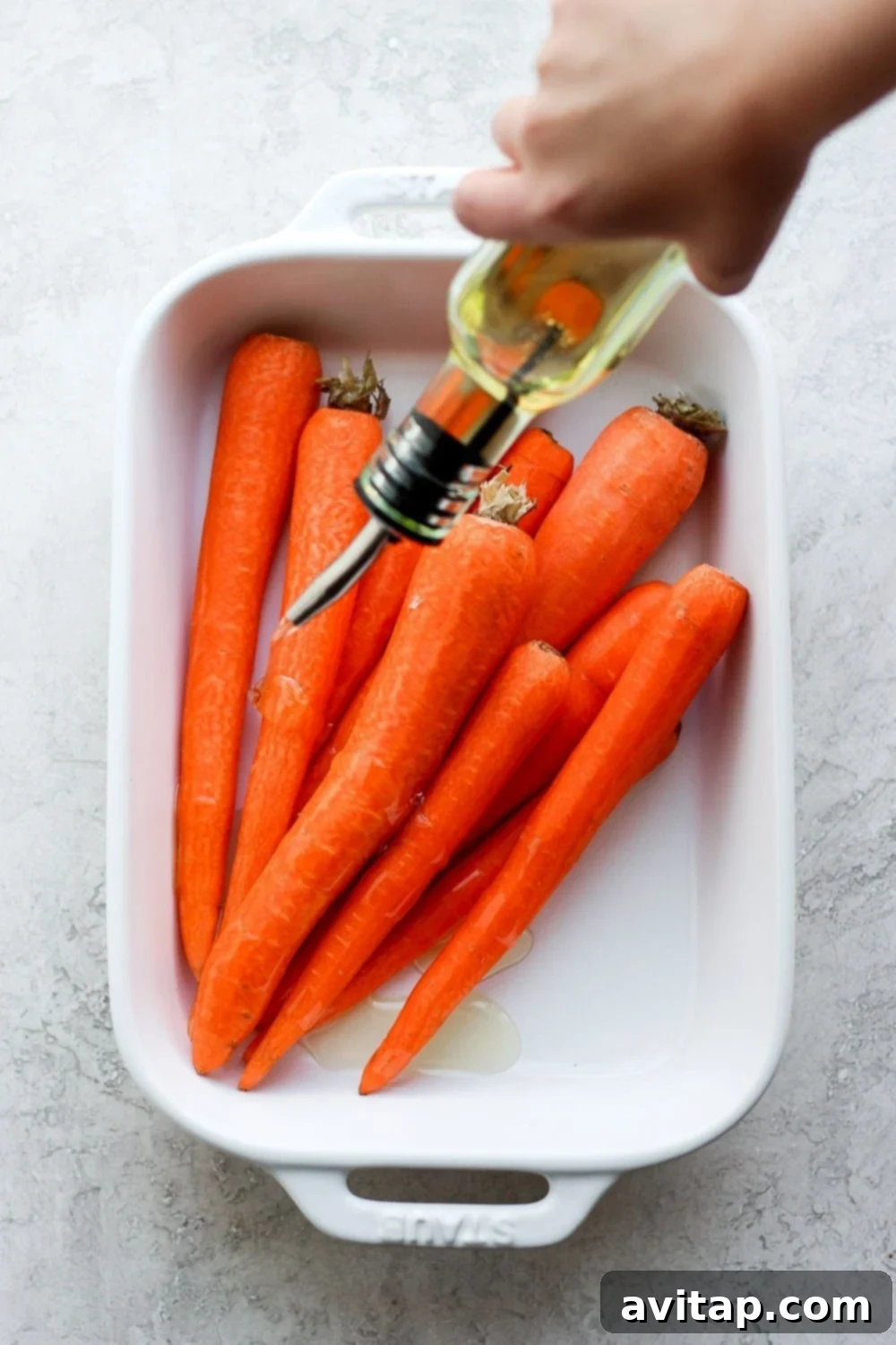 Drizzling olive oil over fresh carrots before seasoning for grilling