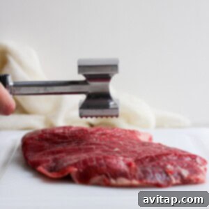 Tenderizing flank steak on a cutting board to ensure even thickness.