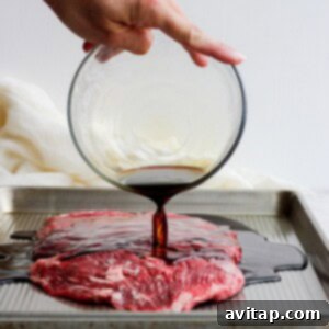 Flank steak marinade being poured over flank steak on a baking sheet.