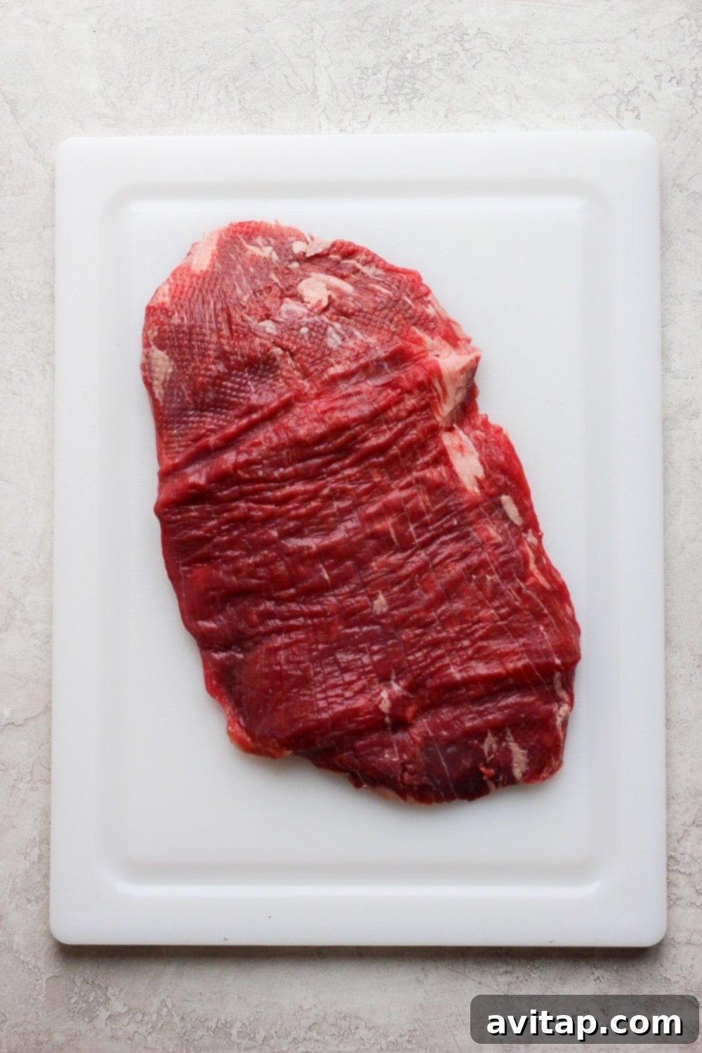 Grill up a flank steak so you can have meal prep flank steak all week long! It's perfect in bowls, for a snack, and everything in between! Pounded flank steak on a cutting board, prepared for marinating.