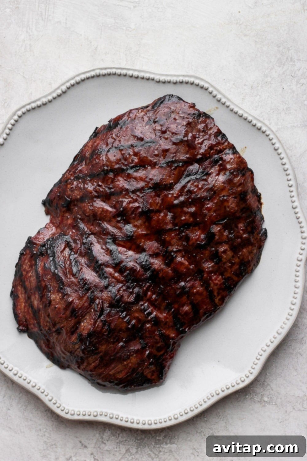 Grilled flank steak is perfect for a weeknight meal! Marinate, grill, and serve! The family will love it! Grilled flank steak on a plate, perfectly sliced into tender strips, ready to be served.