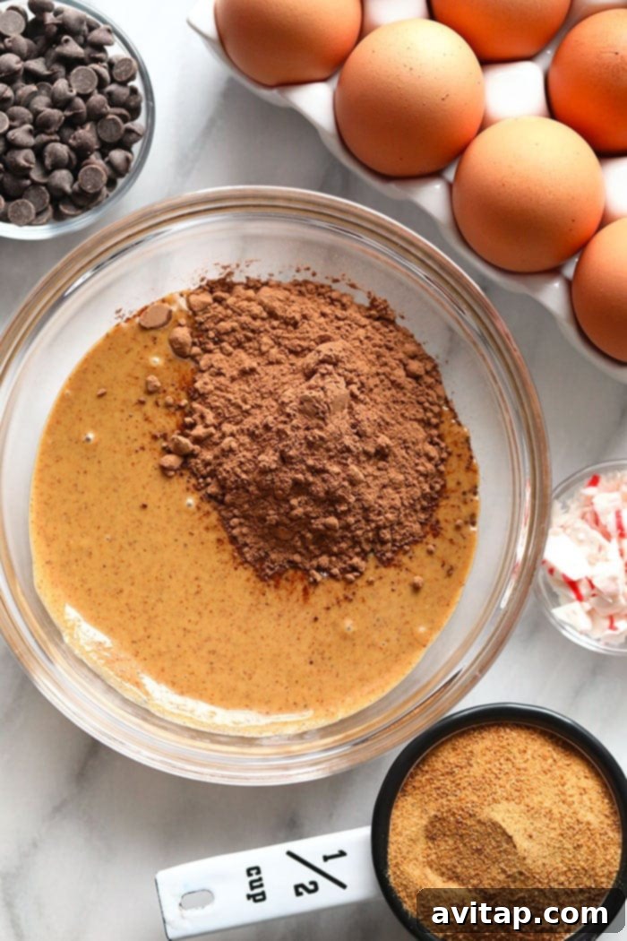 Ingredients for healthy hot cocoa cookies in a mixing bowl, including almond butter, cocoa powder, and coconut sugar.