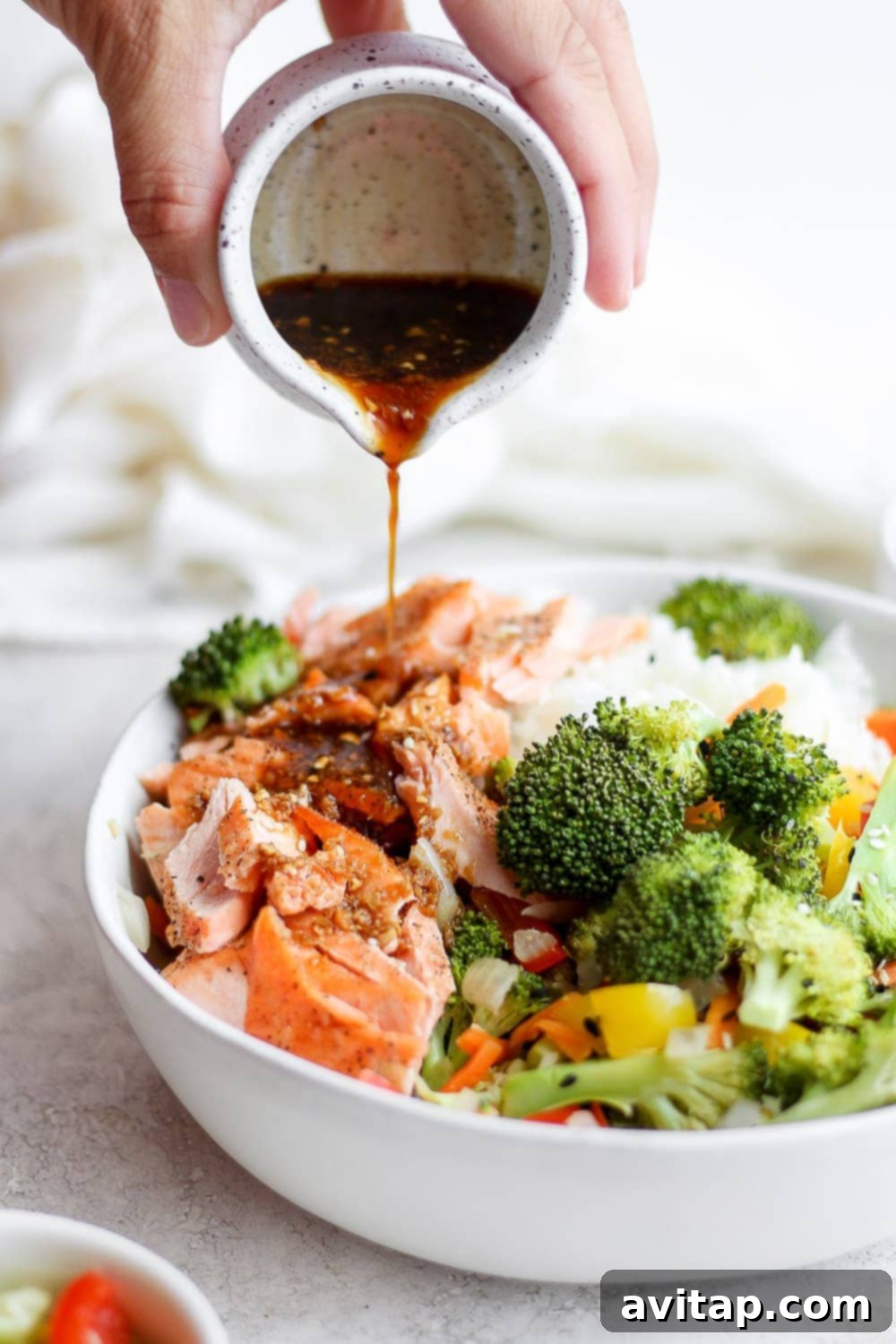 Stir fry sauce being poured over sheet pan salmon stir fry in a bowl