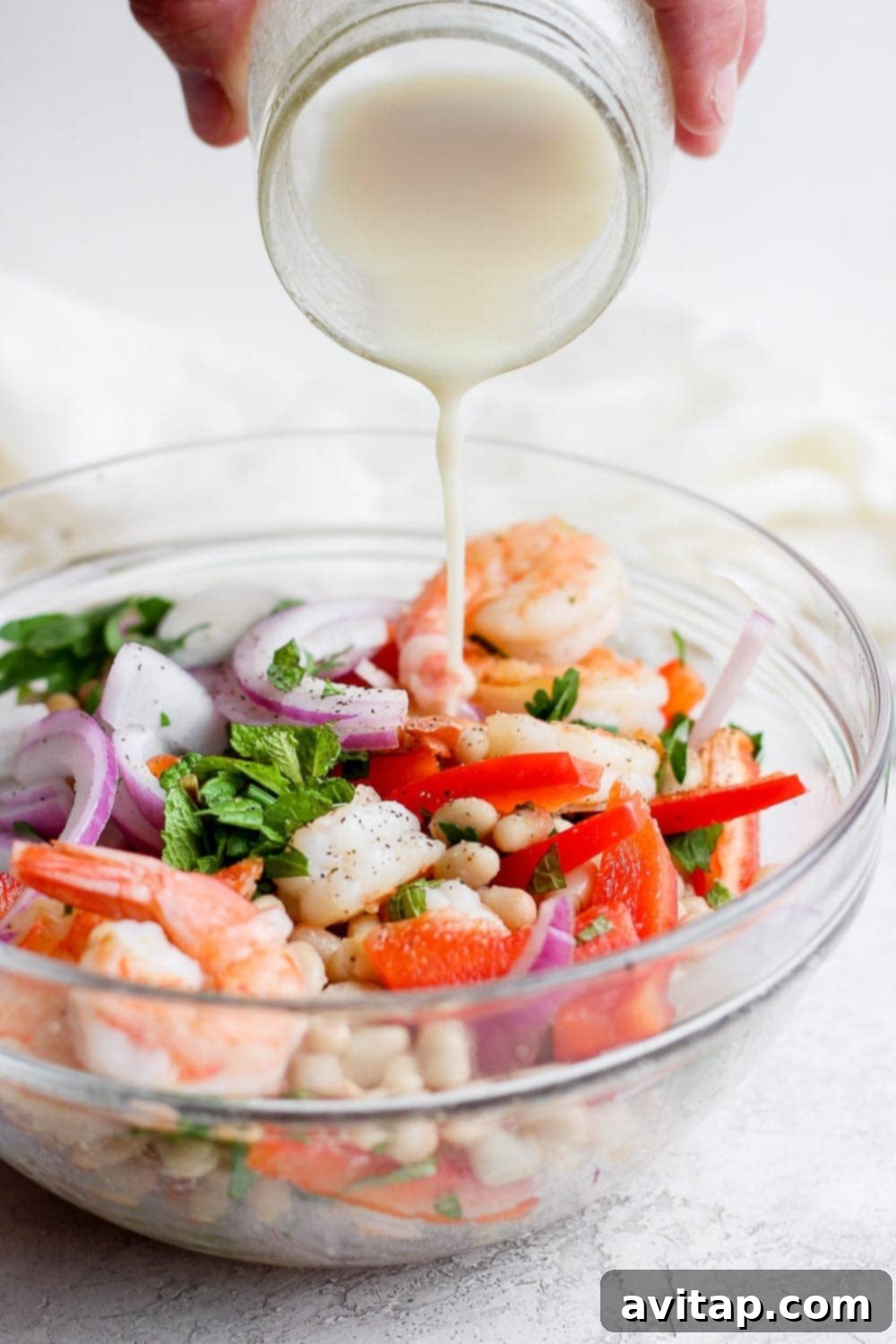 Creamy, homemade dressing being generously poured over a colorful healthy shrimp salad in a bowl