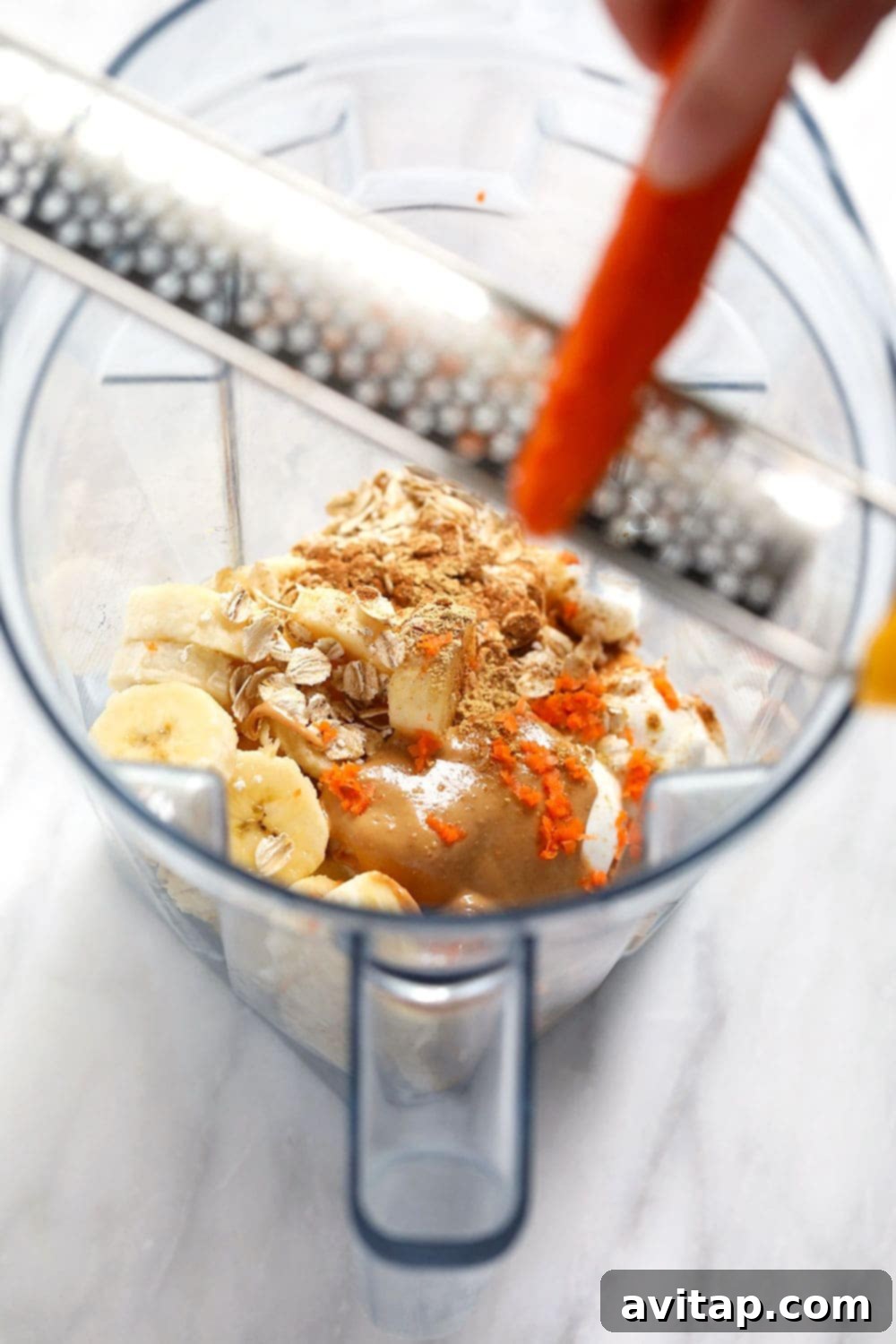 All the whole and healthy ingredients for a carrot cake smoothie are neatly arranged around a high-speed blender.