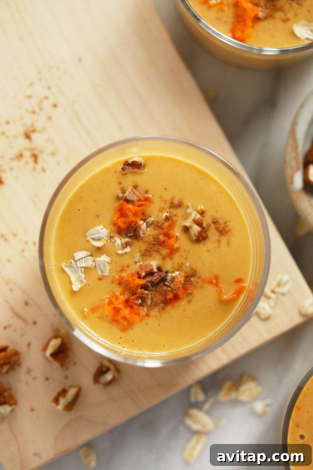 A glass of carrot cake smoothie beautifully topped with chopped walnuts, oats, and a sprinkle of shredded carrot, ready to be enjoyed.