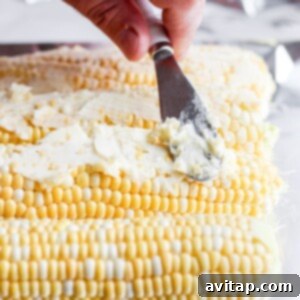 a person slicing grilled corn on the cob with a knife.