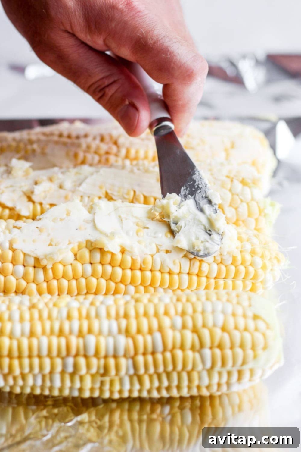 softened butter being spread on ears of corn before it goes on the grill
