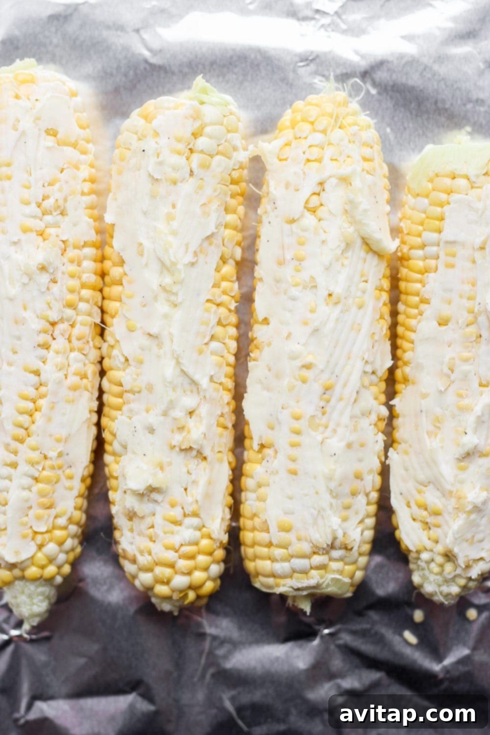 corn on the cob with butter spread on it, laid atop tin foil and ready to be made into a foil pack