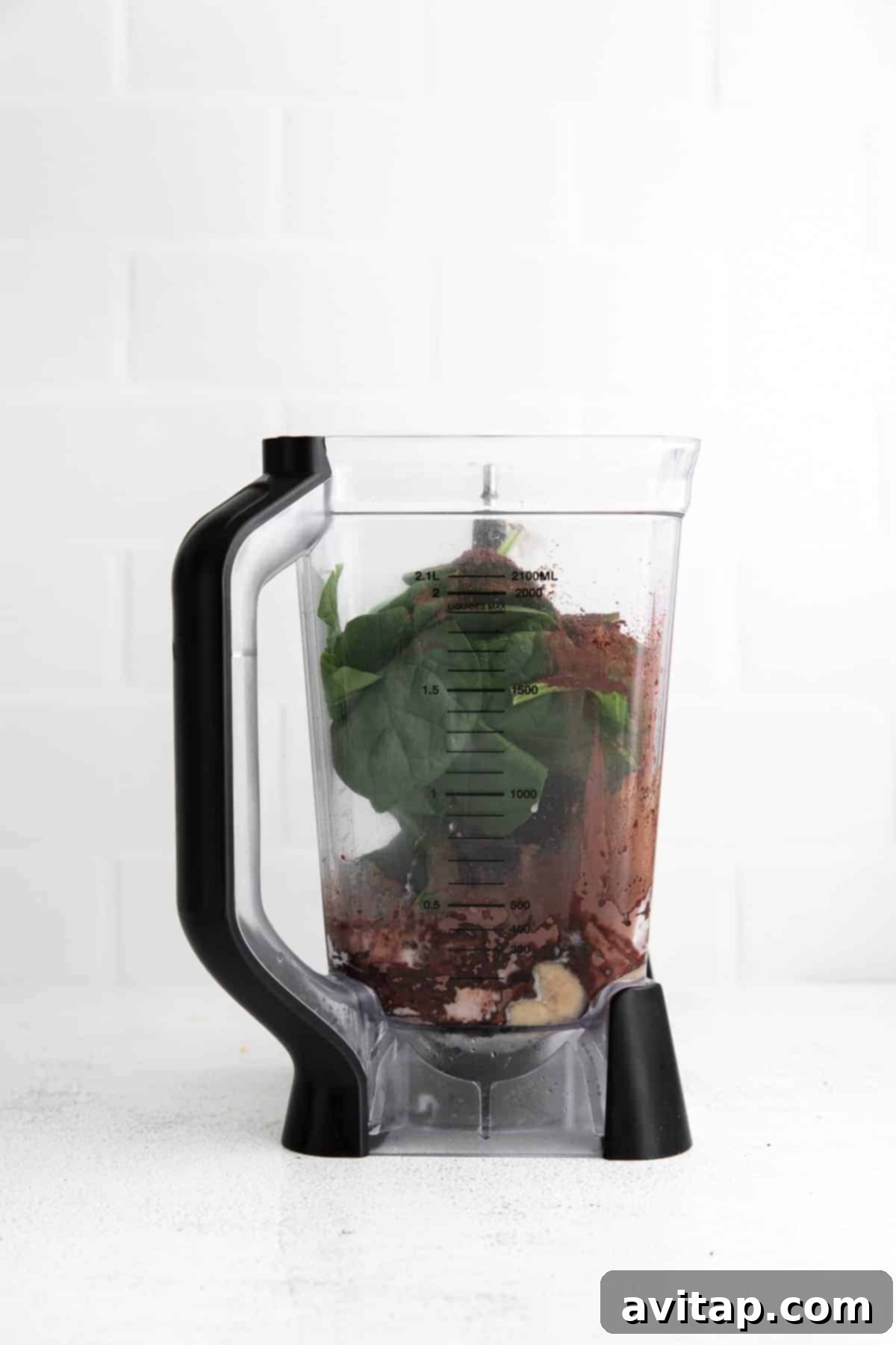 All the smoothie ingredients, including frozen bananas, peanut butter, spinach, and milk, placed inside a blender, ready for blending.