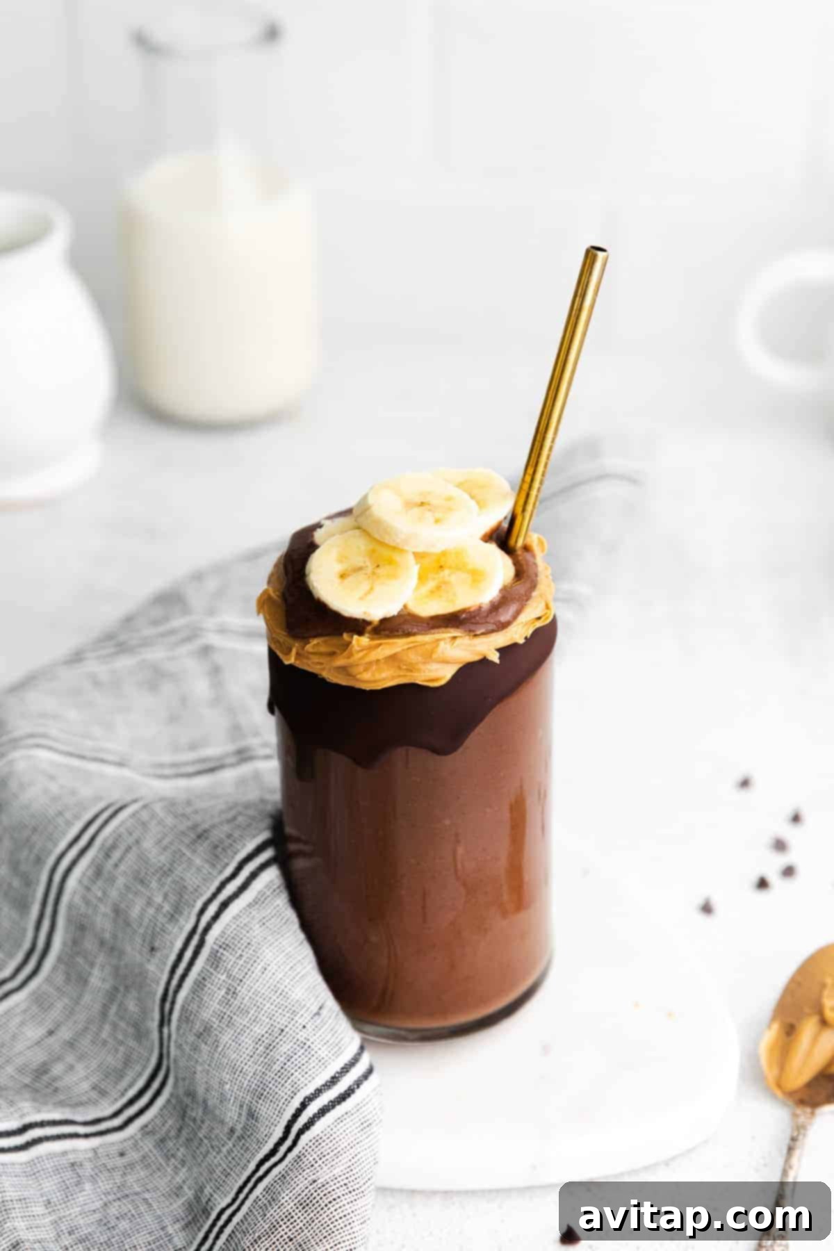 A chocolate peanut butter banana smoothie topped with a drizzle of peanut butter and fresh banana slices, served in a glass with a straw.