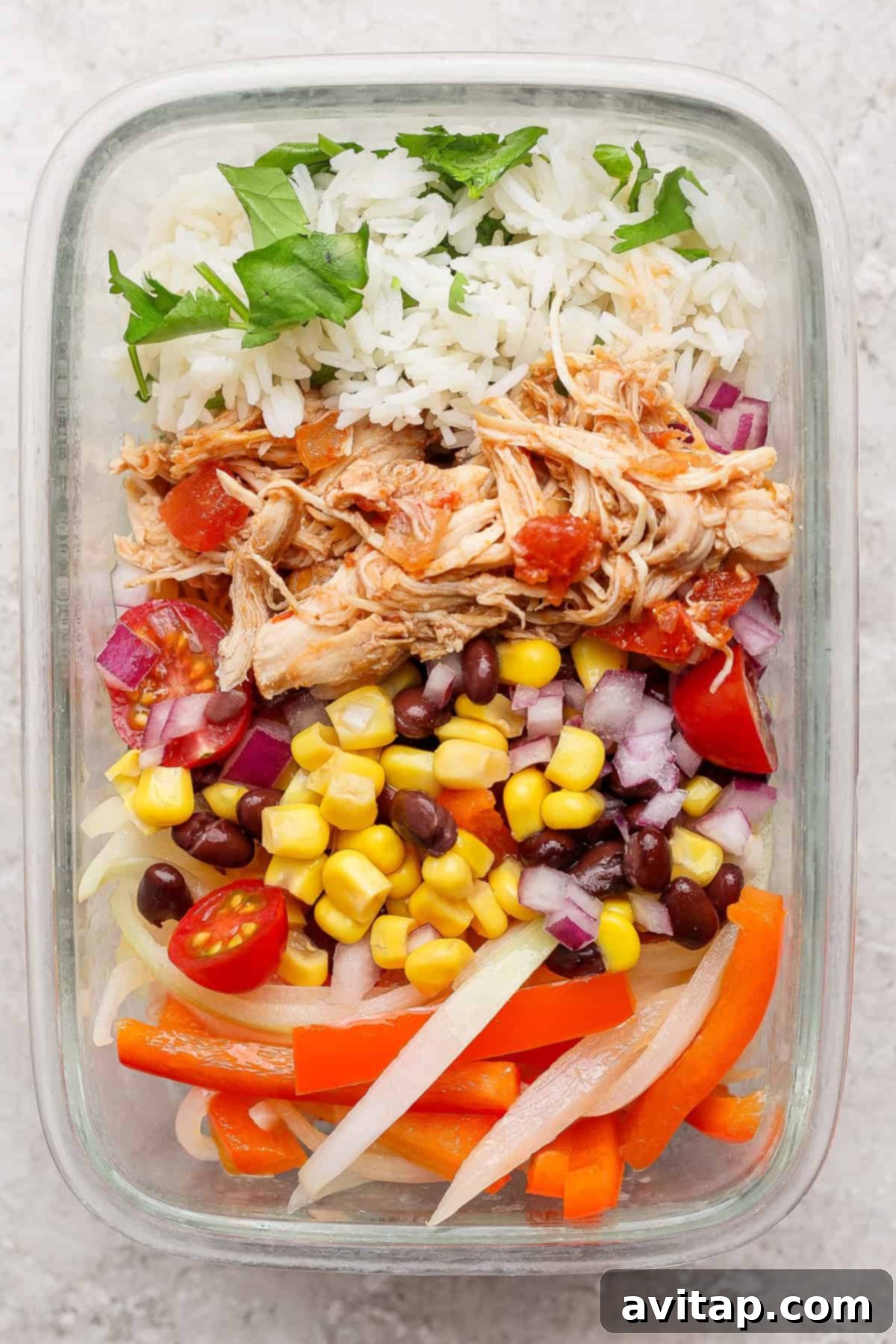 A meticulously prepared glass meal-prep container filled with fluffy rice, savory shredded chicken, hearty black beans, sweet corn, crisp red onions, juicy cherry tomatoes, colorful sliced bell peppers, and fresh cilantro, ready for a healthy meal.