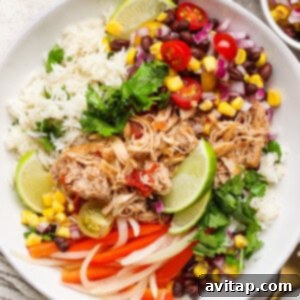 A bowl filled with shredded chicken, fluffy rice, black beans, corn, red onion, tomatoes, lime wedges, fresh cilantro, and vibrant sliced bell peppers, making a complete salsa chicken meal.