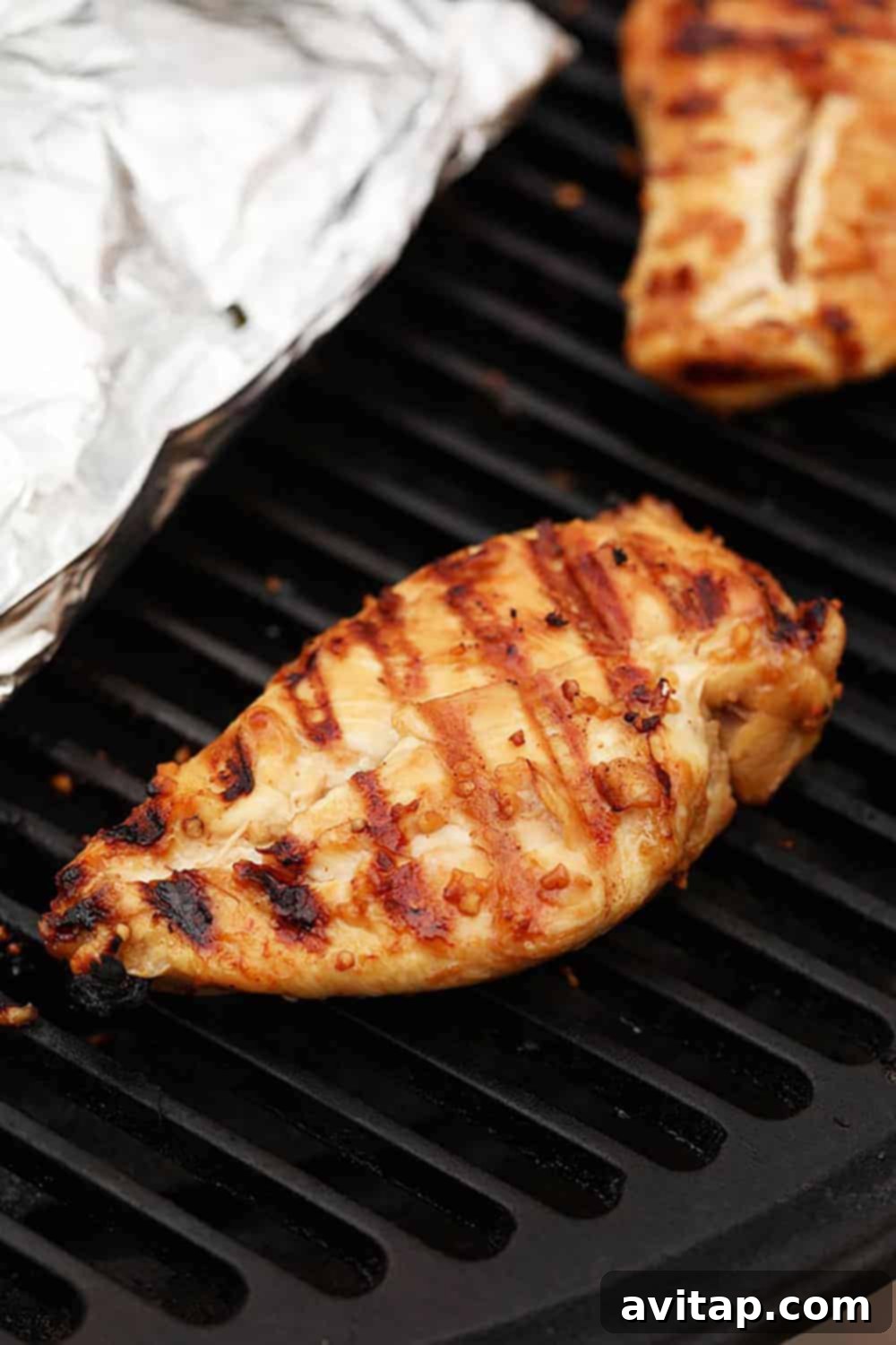 Succulent Grilled Chicken 5 Close-up view of chicken breasts cooking on a hot grill, showing developing grill marks.