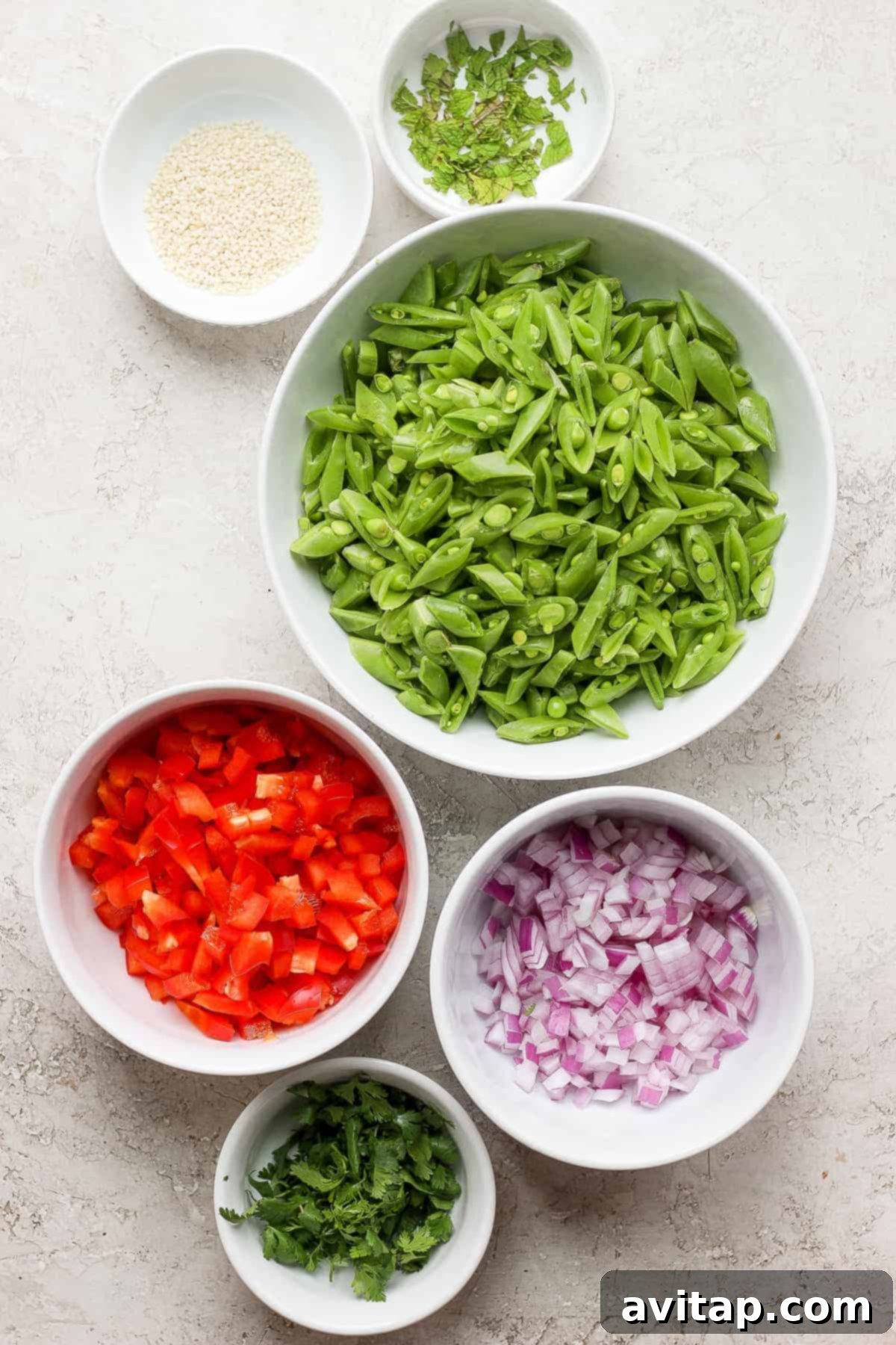 Zesty Ginger Pea Salad 3 Individual bowls holding various ginger pea salad ingredients: sugar snap peas, diced red bell peppers, minced red onion, sesame seeds, and fresh mint leaves.