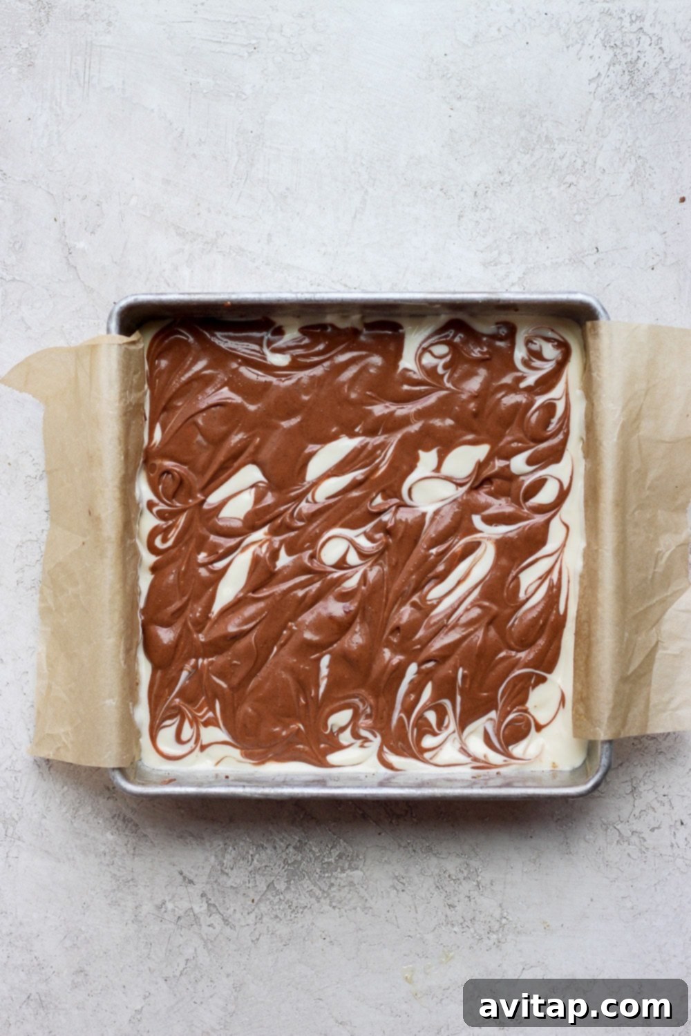 The chocolate chai cheesecake bars, perfectly swirled and resting in the baking pan, showcasing the beautiful marbling before they are baked.