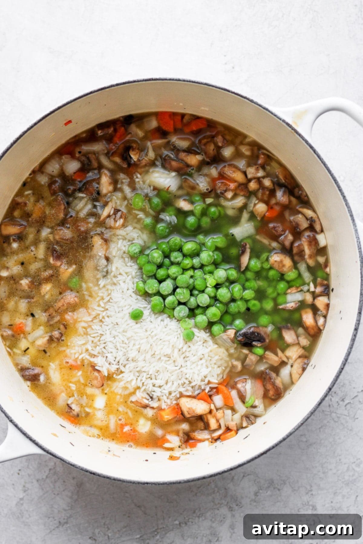 A stockpot filled with rice, chicken broth, and a vibrant mix of vegetables, ready for the chicken to be added and baked.