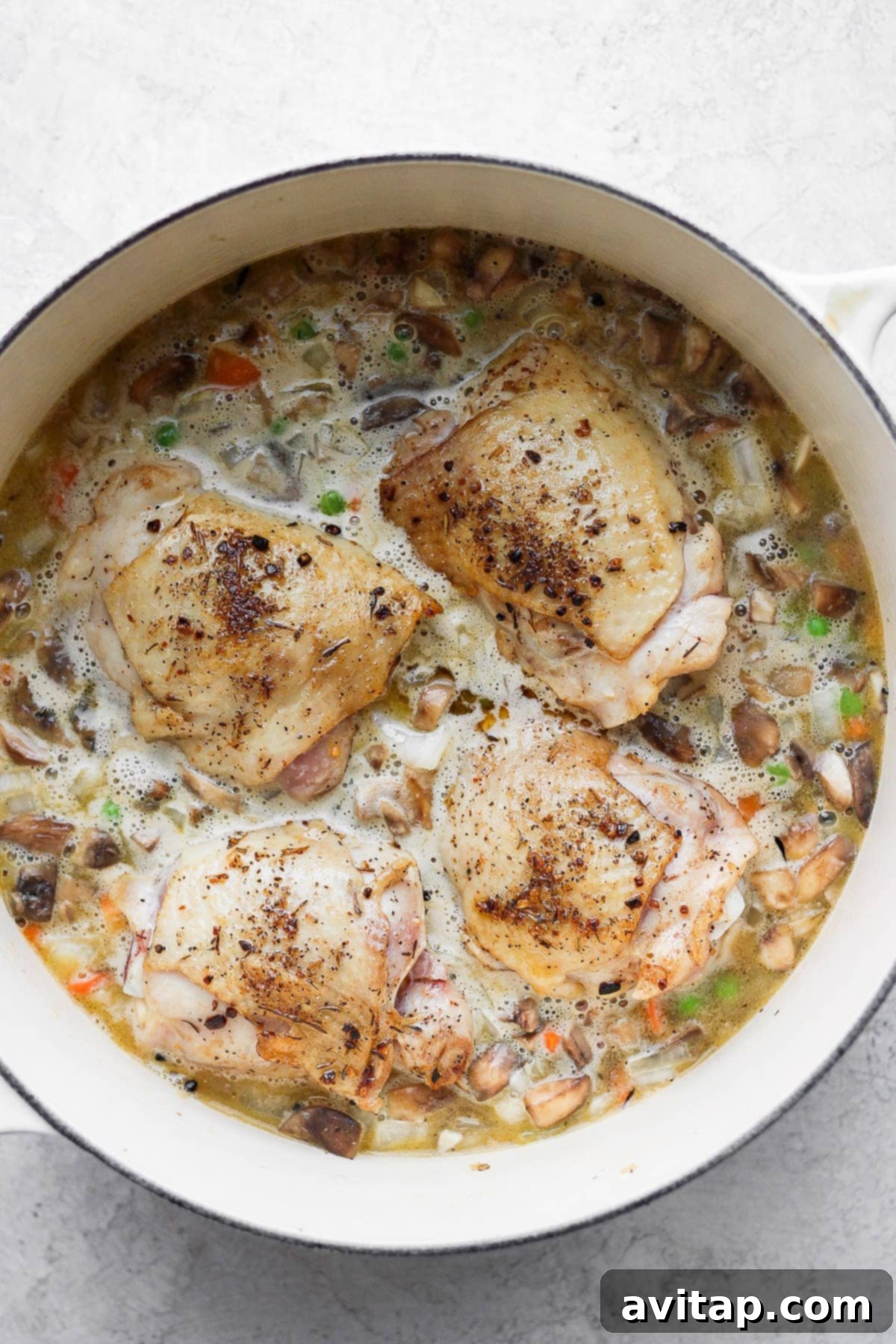 Uncooked rice mixture with perfectly seared chicken thighs arranged on top, ready for baking in a Dutch oven.