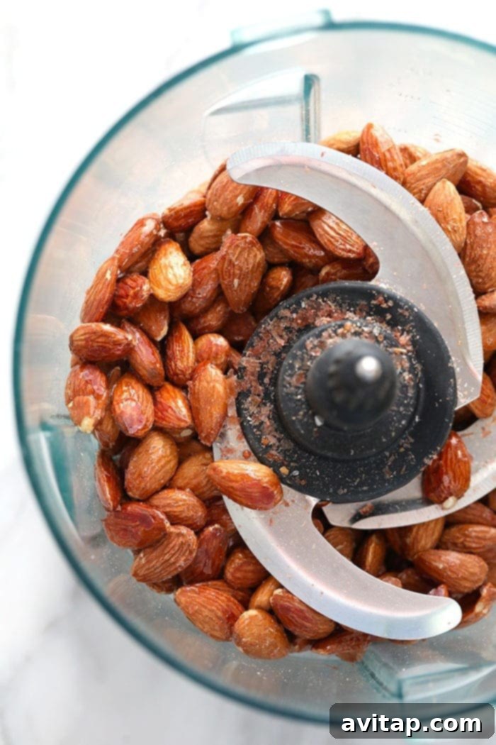 Roasted almonds being processed in a food processor, transforming into almond butter.