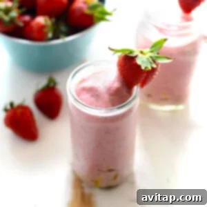 strawberry smoothie with pineapple chunks with strawberry on rim of glass
