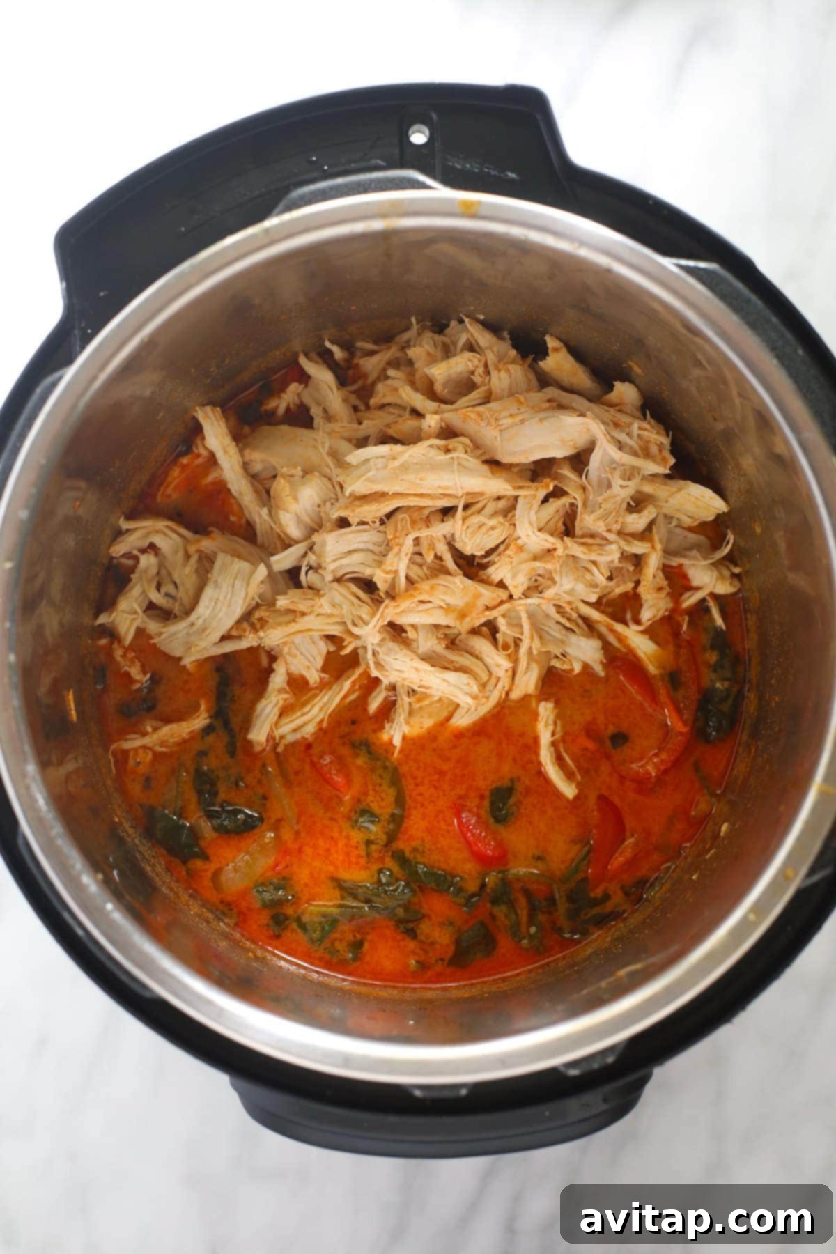 Close-up of coconut curry chicken cooking inside an Instant Pot, showing the vibrant colors of the sauce and chicken.