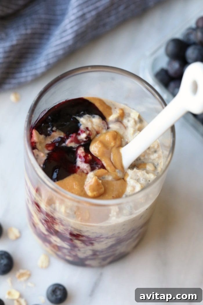 Close-up of creamy overnight oats with a swirl of red jelly and peanut butter, garnished with fresh berries.