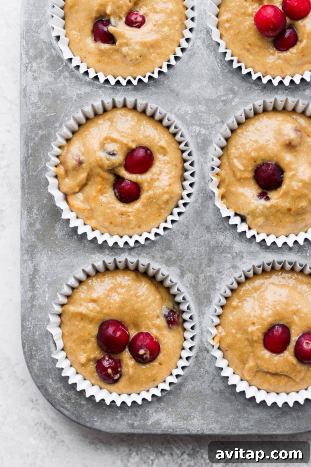 Cranberry orange muffin batter carefully scooped into a muffin tin lined with paper cups, ready for baking.