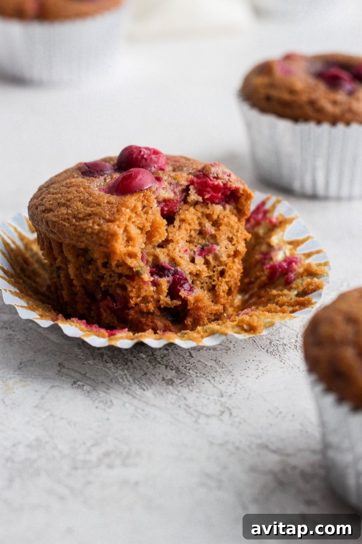 A healthy cranberry orange muffin with a bite taken out, revealing its fluffy interior and vibrant cranberry pieces.