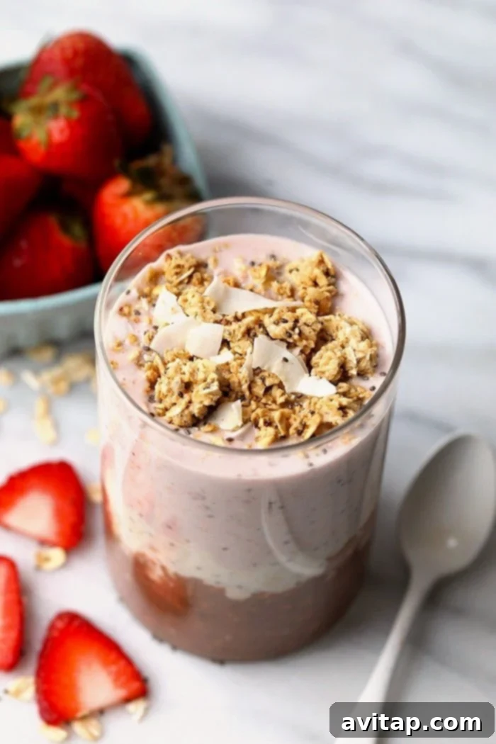 Overhead photo of Neapolitan overnight oats served in a glass jar, elegantly garnished with fresh whole strawberries and sliced berries in the background.