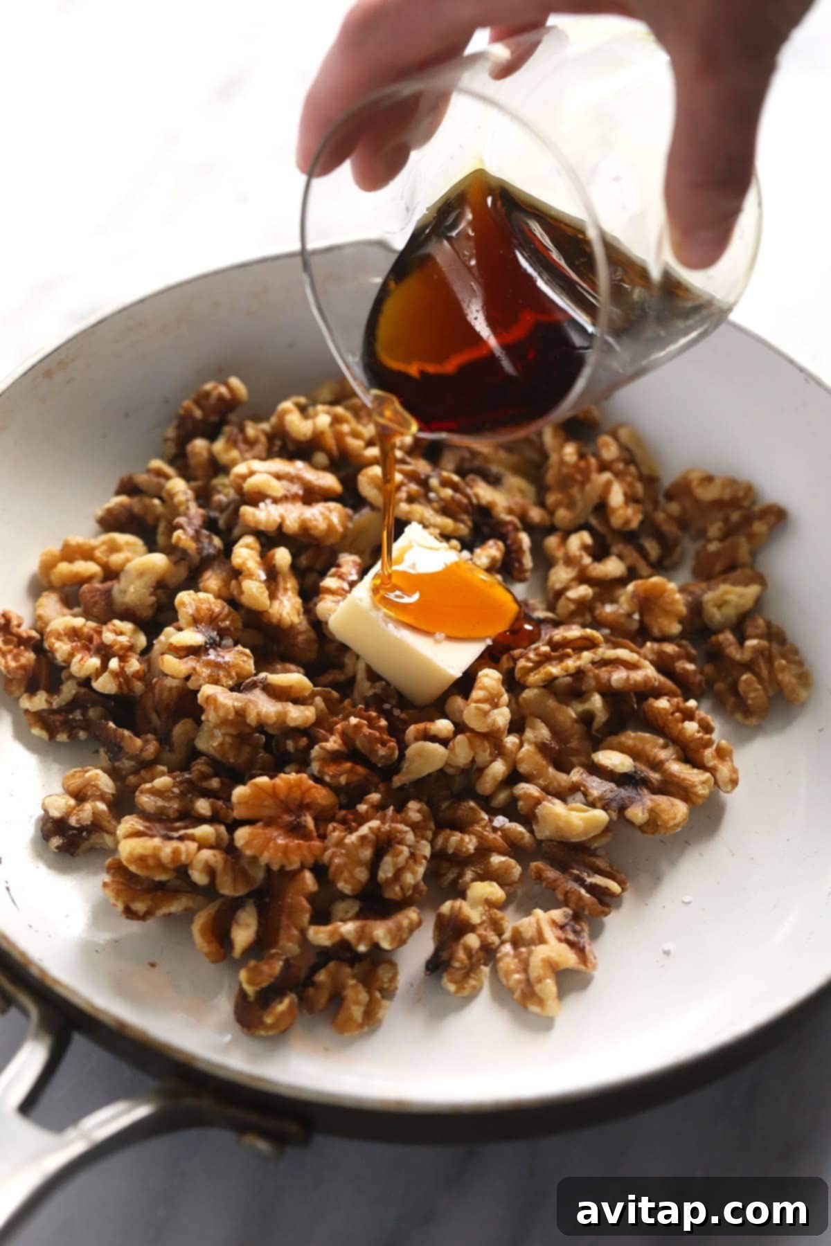 Simply Delicious Candied Walnuts 3 Maple syrup being poured into a hot pan with walnuts, starting the candying process.