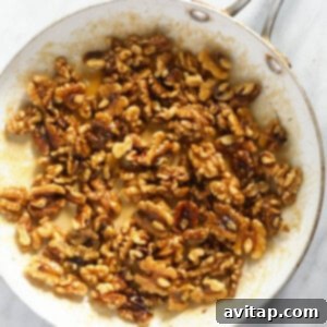 Walnuts coated in maple syrup and butter, simmering in a frying pan on a marble countertop, developing their candied glaze.