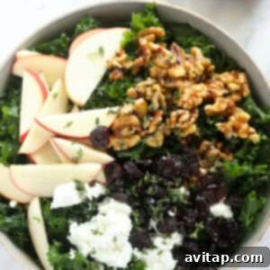 A finished Thanksgiving salad in a large bowl, garnished with kale, apple slices, and walnuts.