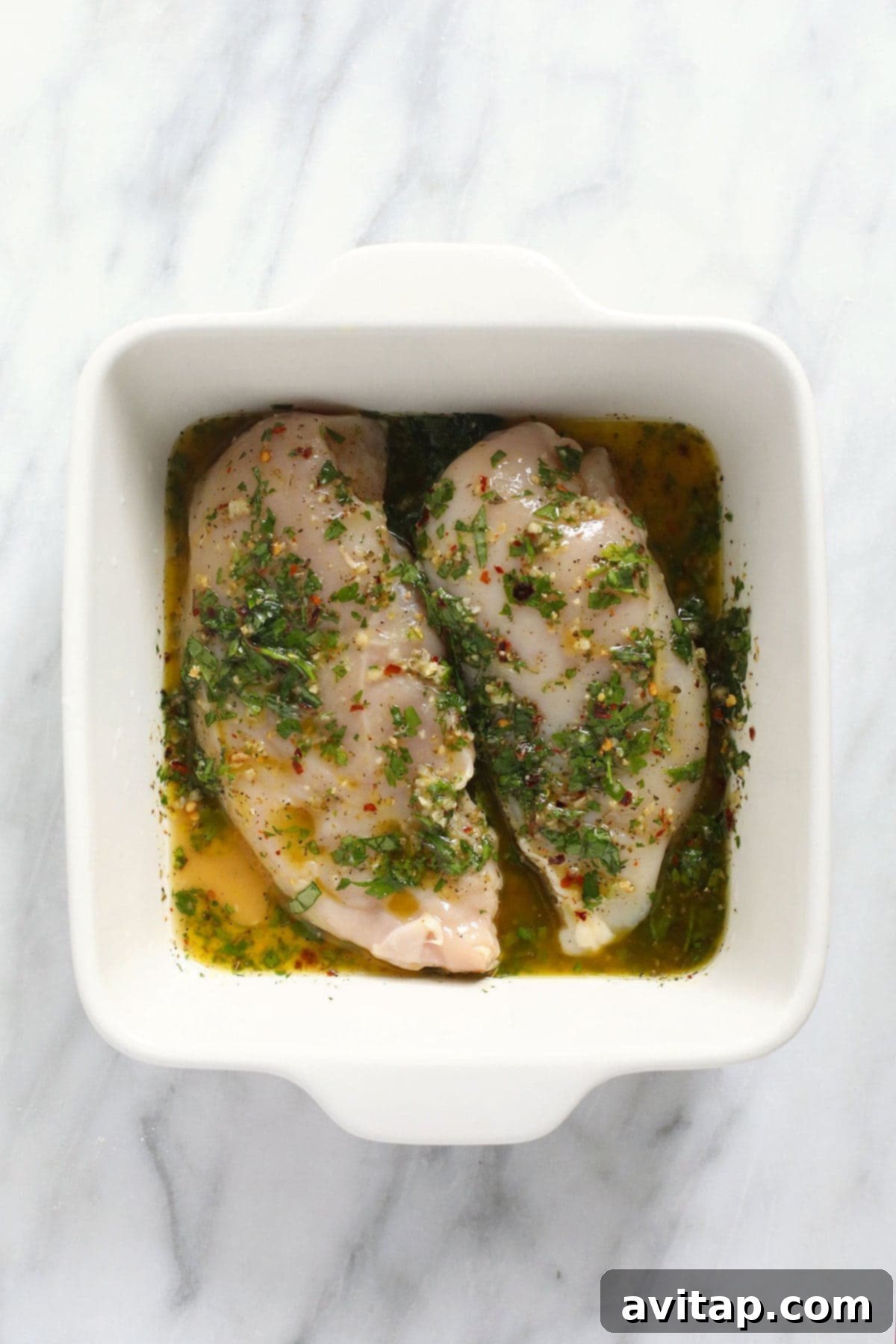 Chicken breasts marinating in an Italian dressing in a shallow white dish.