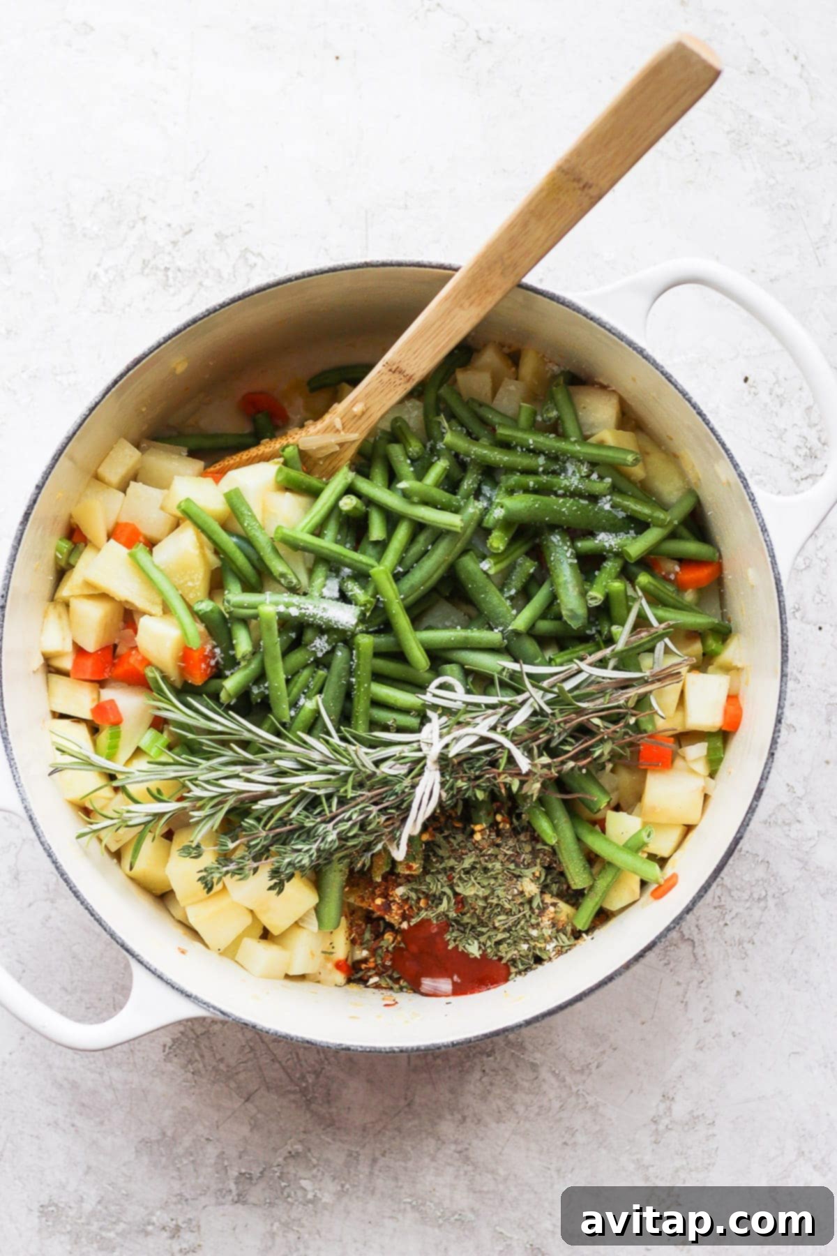 All the fresh ingredients for vegetable soup, including various colorful vegetables, herbs, and spices, gathered in a Dutch oven before cooking.