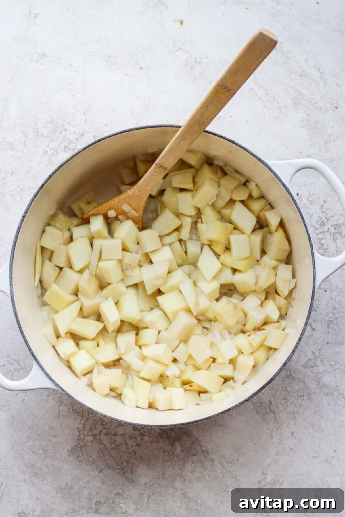 Diced potatoes, onions, and minced garlic simmering in olive oil in a large Dutch oven, creating the fragrant flavor base for the soup.
