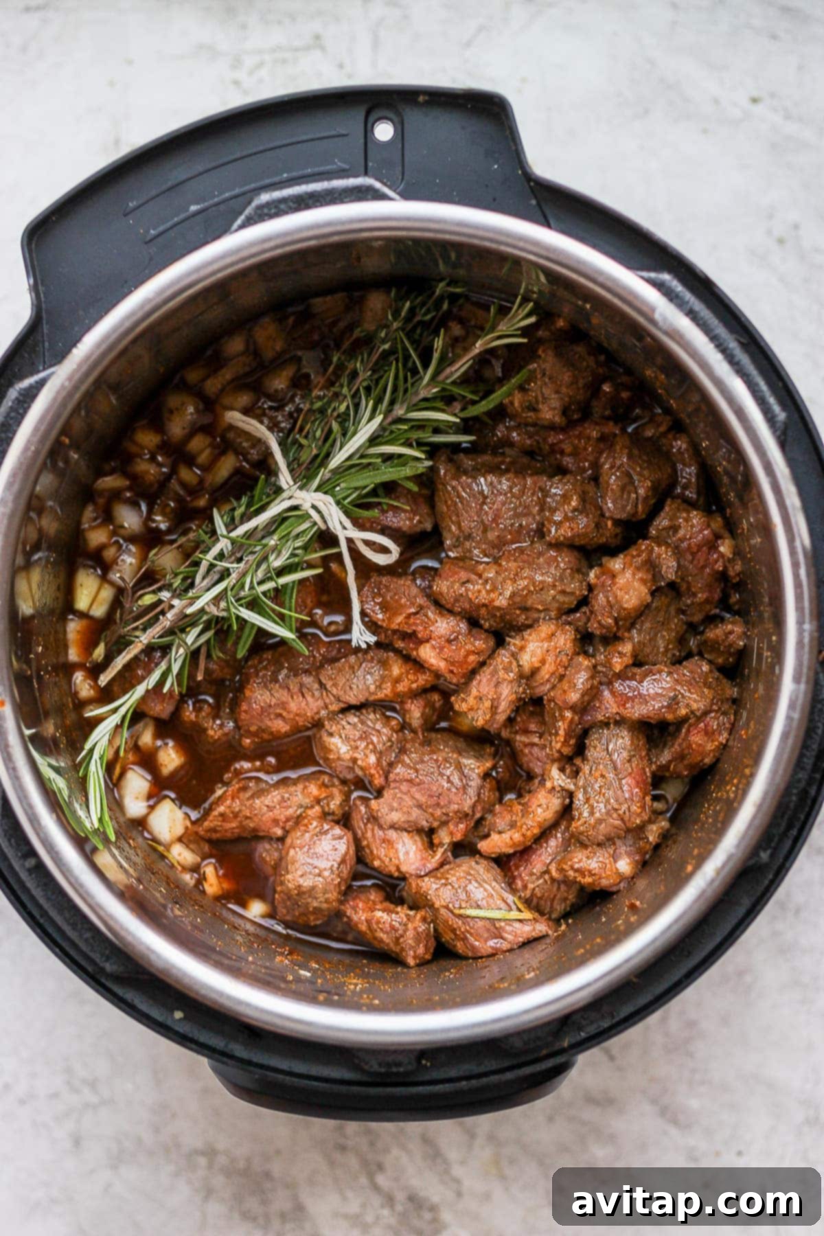 Instant Pot beef stew simmering, with a fresh herb bundle of rosemary and thyme infusing fragrant notes into the rich broth.