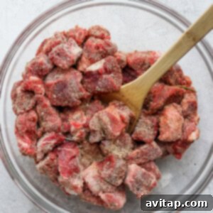 Instant pot shredded beef stew in a glass bowl with a wooden spoon.