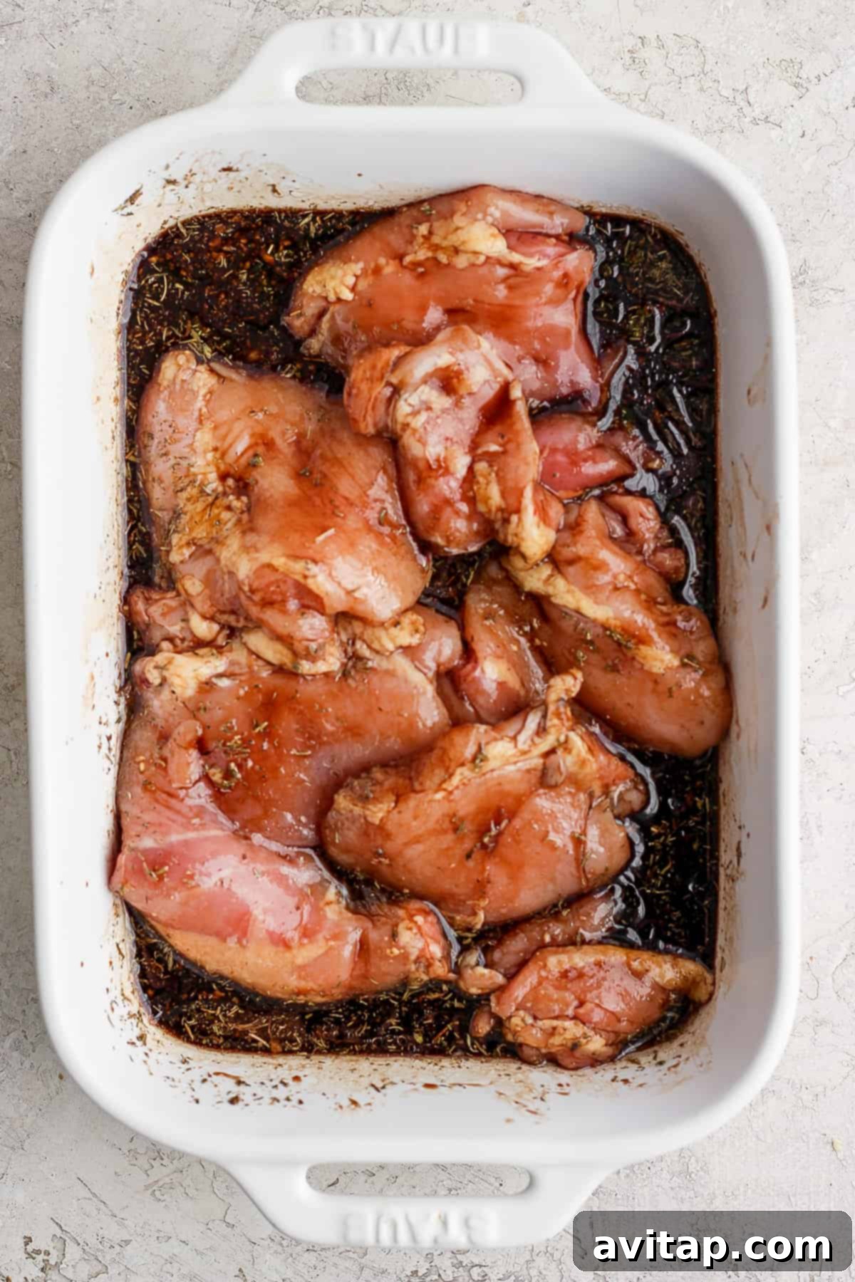 Raw chicken breasts resting in a white baking dish, thoroughly coated in a rich marinade.