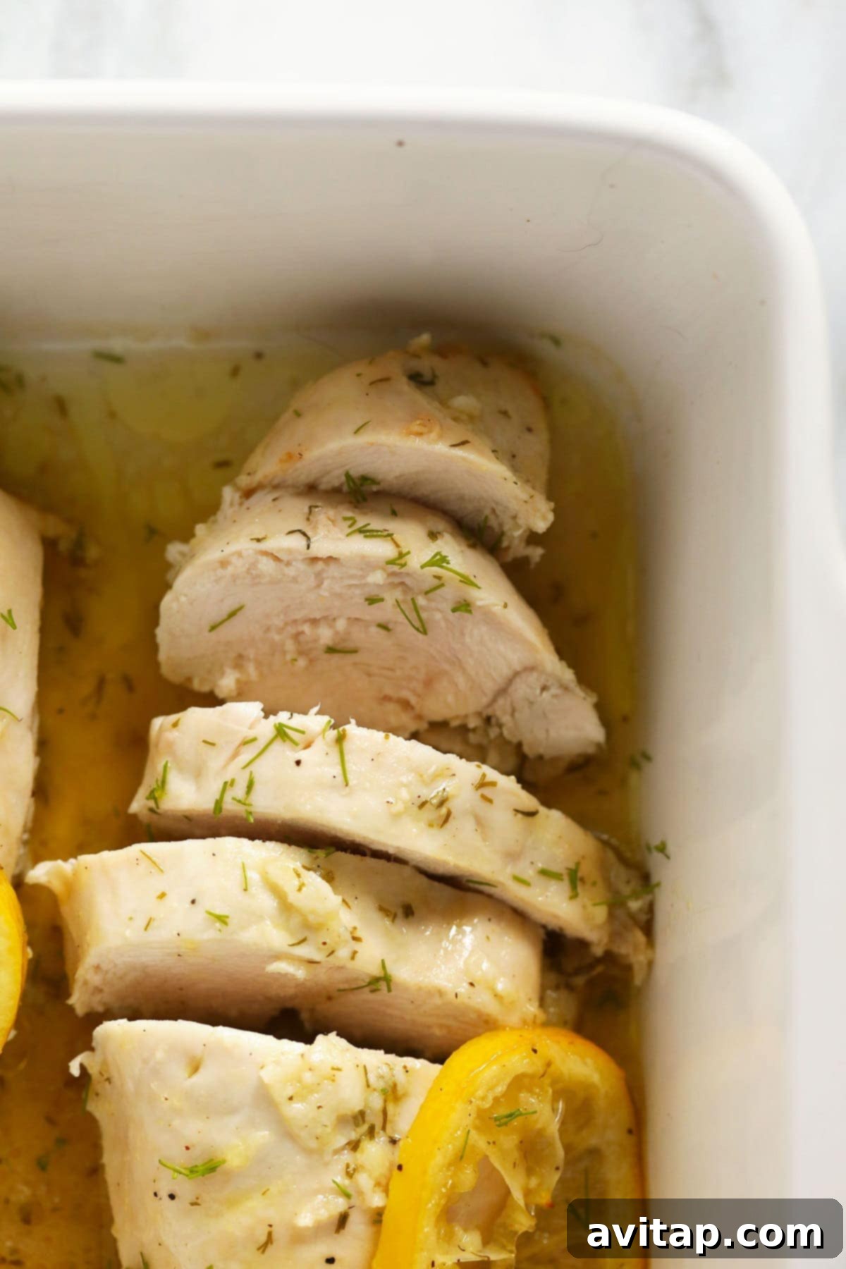 Beautifully cooked and artfully sliced lemon chicken breasts presented in an elegant white baking dish.
