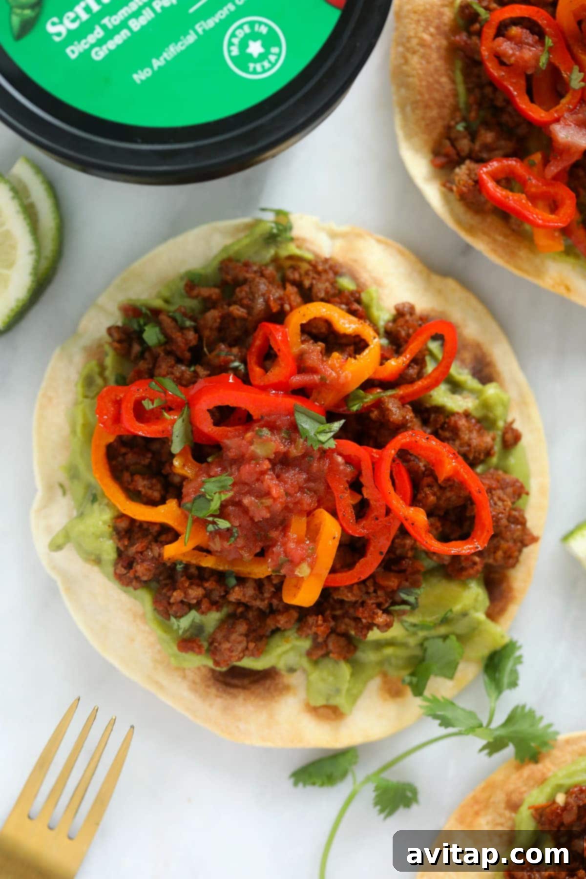 Fully assembled vegetarian tostada with creamy guacamole, plant-based ground, vibrant peppers, and a drizzle of salsa