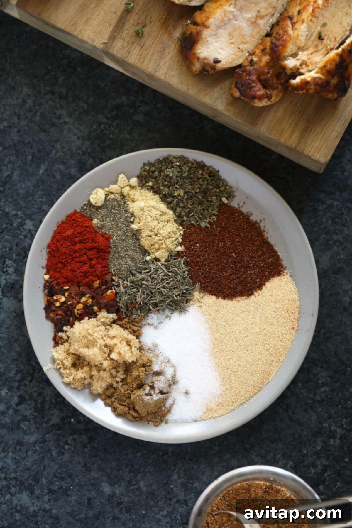 A vibrant display of various dried spices and herbs arranged neatly on a plate, ready to be mixed into the ultimate chicken seasoning blend.