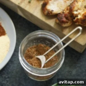 A close-up of various spices being stirred together in a glass jar to form the chicken seasoning.