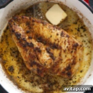 A frying pan with a piece of chicken searing, showing the butter and golden crust forming.