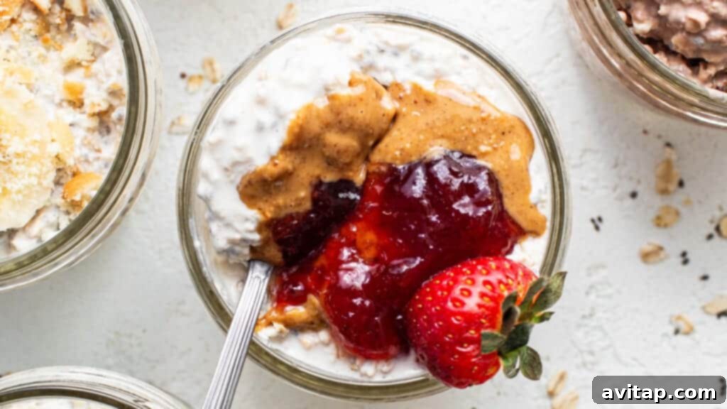 A bowl of peanut butter and jelly overnight oats, topped with fresh strawberries and a swirl of jelly.