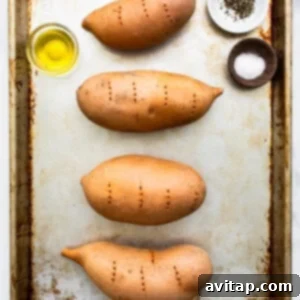Four sweet potatoes on a baking sheet with olive oil and spices.